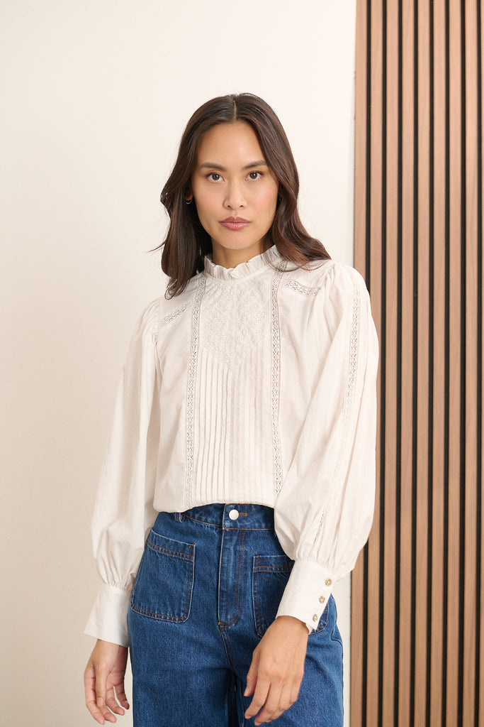 Femme portant la blouse BELLA coloris blanc, une blouse ample en voile de coton avec découpe composée de dentelle et plis.