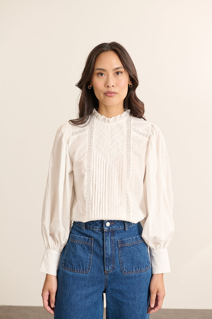 Mannequin femme de face portant une blouse ample blanche en voile de coton, col volanté et empiècements en dentelle.
