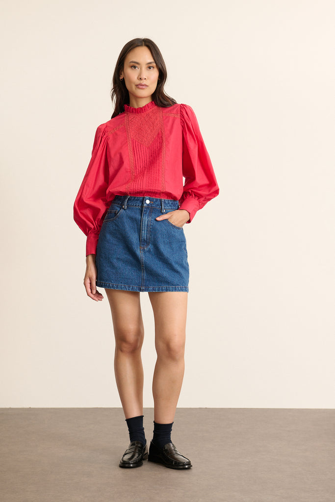 Mannequin femme de face portant une blouse ample cerise en voile de coton, col volanté et empiècements en dentelle.