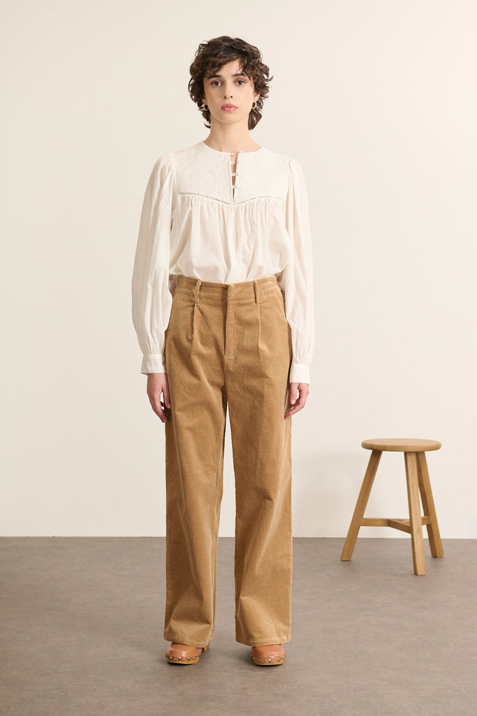 Mannequin femme de face portant une blouse ample coloris blanc en voile de coton, plastron matelassé devant et col rond.