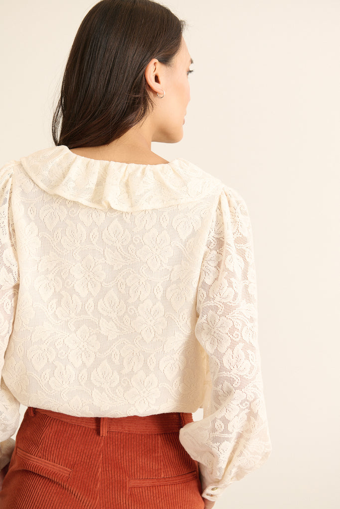 Vue arrière de la blouse en dentelle écrue, coupe droite avec base légèrement arrondie et col volanté visible au dos.