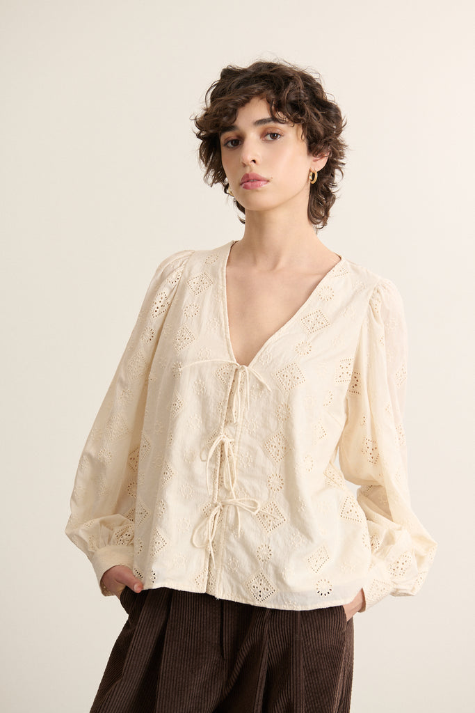 Mannequin femme de face portant une blouse écru en dentelle coton, coupe droite avec encolure dégagée. 