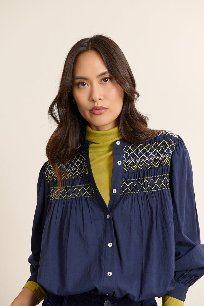 Mannequin femme de face portant une blouse ample coloris marine en voile de coton, découpe matelassée sur le devant.