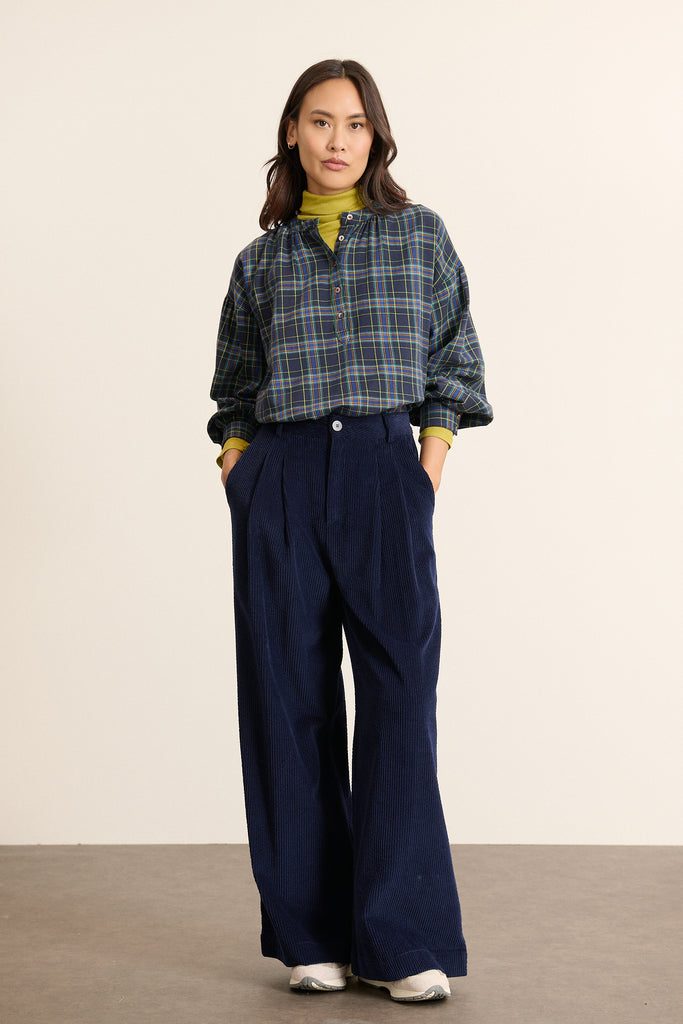Mannequin femme de face portant une blouse ample à carreaux marine, coupe droite avec encolure dégagée, fermeture boutonnée. 