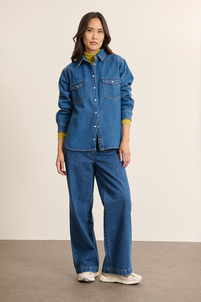 Mannequin femme de face portant une chemise en denim bleu 100 % coton, coupe droite avec poches poitrine à rabats. 