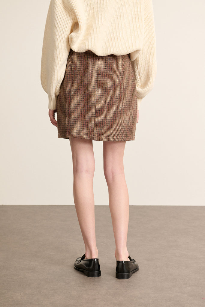 Coloris marron, la mini jupe BOWEN est fabriquée en laine et polyester avec un tissu esprit pied de poule. 