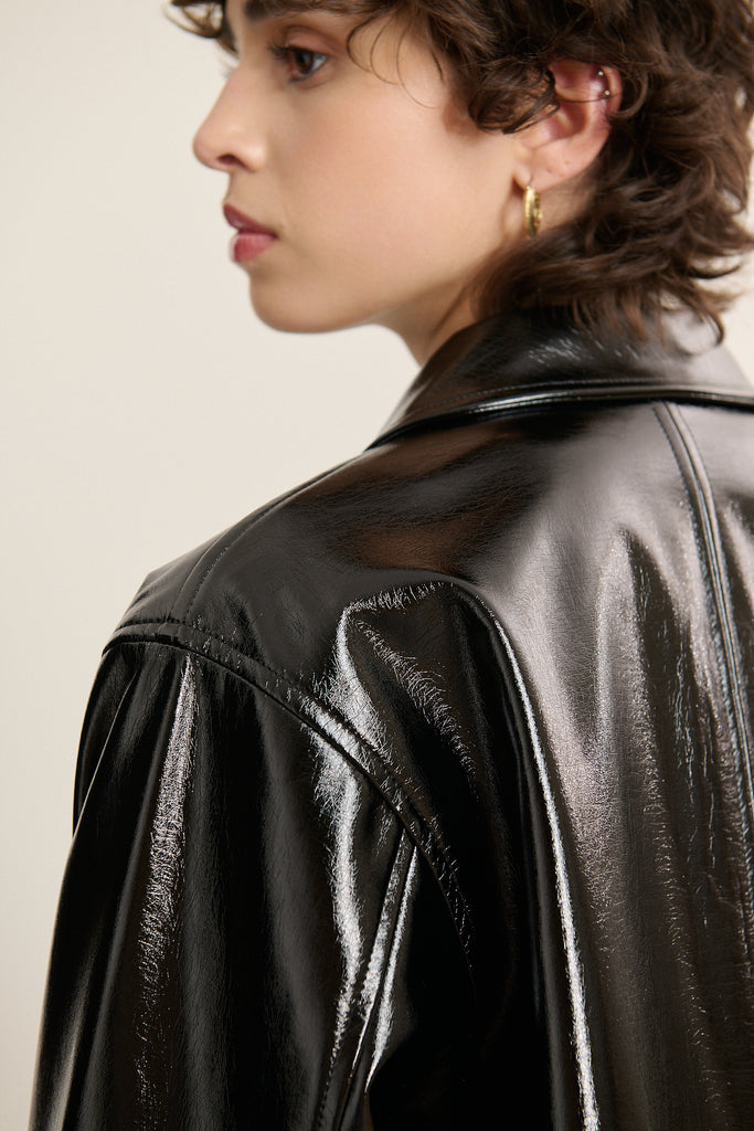 Focus sur la matière vinyle brillante, texture lisse effet miroir pour une silhouette assumée avec bouton pression recouvert.