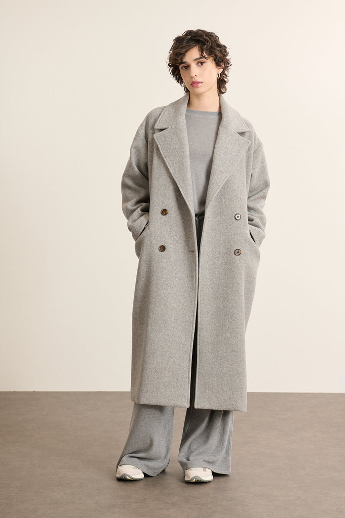 Manteau long coloris gris porté par une femme, à la coupe droite et à l'allure contemporaine style Garance Paris. 