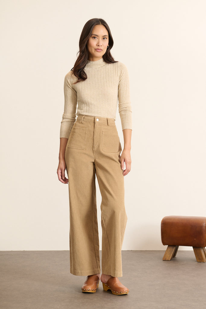 Mannequin femme de face portant un pantalon en velours milleraies beige, coupe droite avec ceinture plate et poches devant. 