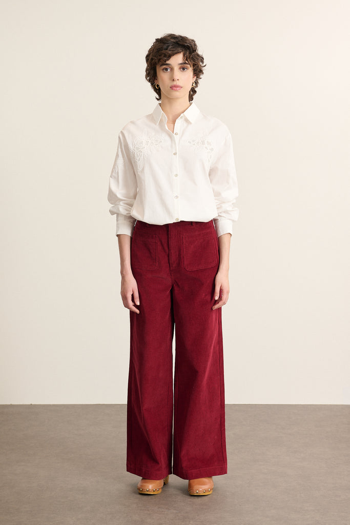 Mannequin femme de face portant un pantalon en velours milleraies grenat, coupe droite avec ceinture plate et poches devant. 