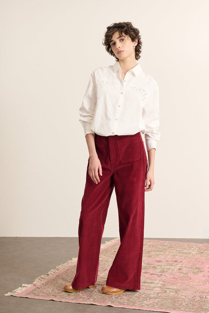 Femme portant un pantalon coloris grenat Garance Paris à la coupe droite et aux poches plaquées devant et derrière.