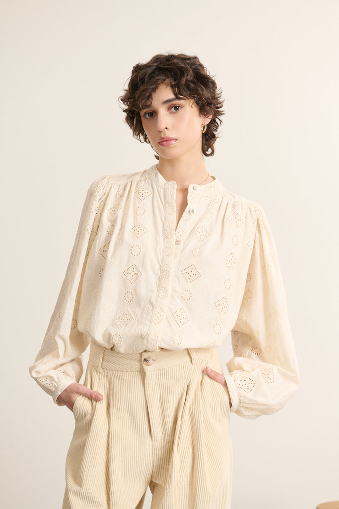 Mannequin femme de face portant une blouse ample coloris écru en dentelle, coupe droite avec col rond et manches longues.