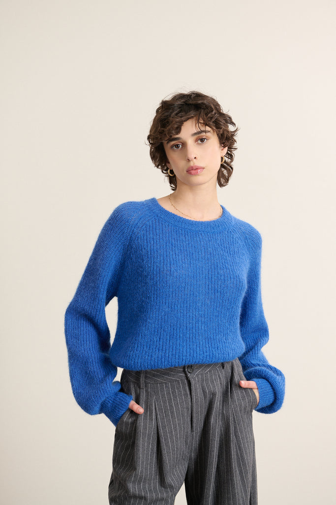 Mannequin femme de face portant un pull ample coloris bleu électrique, col rond, emmanchure raglan et boutonnage dans le dos.