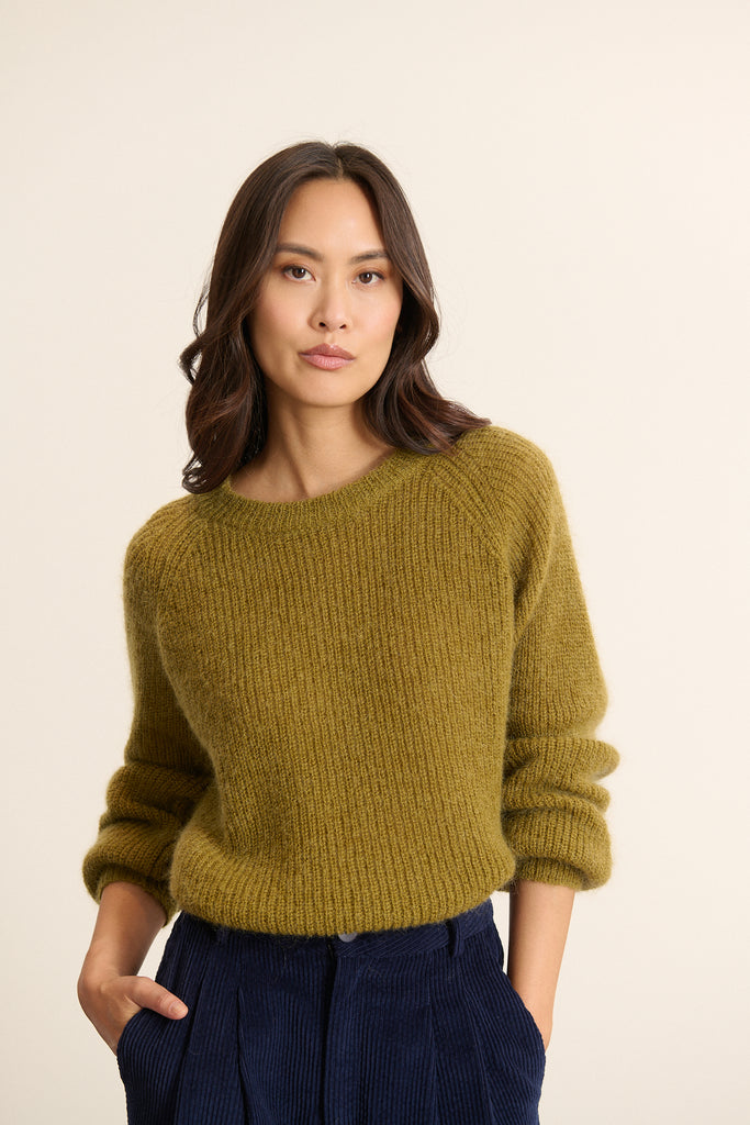 Mannequin femme de face portant un pull ample coloris olive, col rond, emmanchure raglan et boutonnage dans le dos.