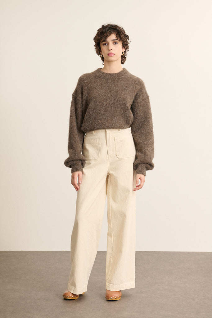 Le pull au volume ample sur le haut du corps, resserré à la taille par un large bord-côte qui structure la silhouette.
