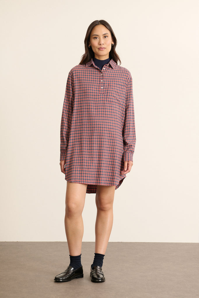 Mannequin femme de face portant une robe chemise courte à carreaux rouges, coupe droite avec poche poitrine et col chemise. 