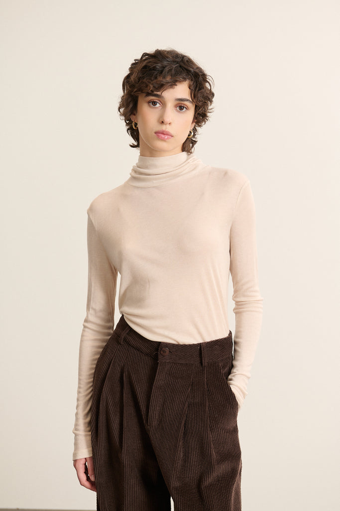 Mannequin femme de face portant un sous-pull beige à col montant, coupe ajustée et manches longues en maille fine. 