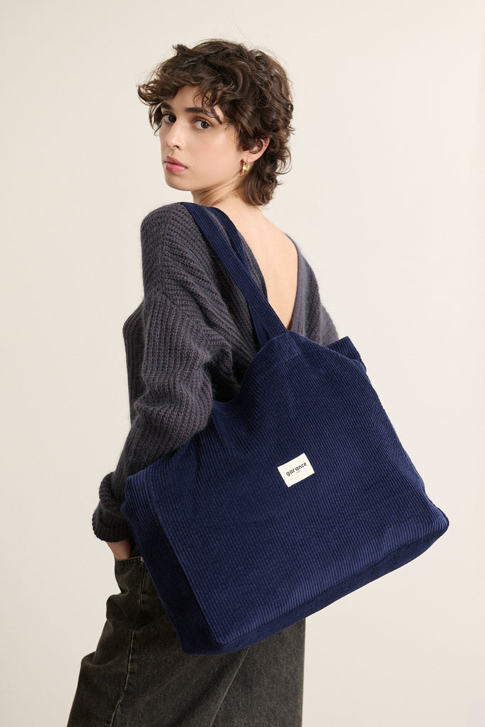 Velours côtelé épais et doux au toucher, coloris marine profond avec tissage dense et finitions surpiquées visibles. 