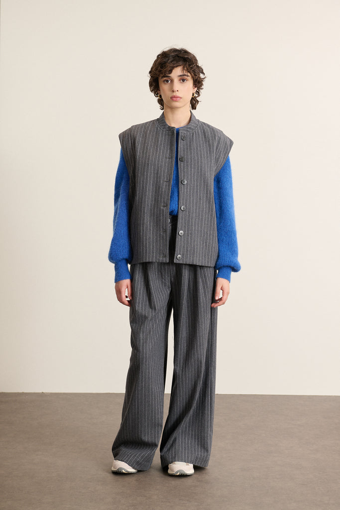 Mannequin femme de face portant une veste sans manches grise à rayures, coupe droite avec col rond et poches plaquées.