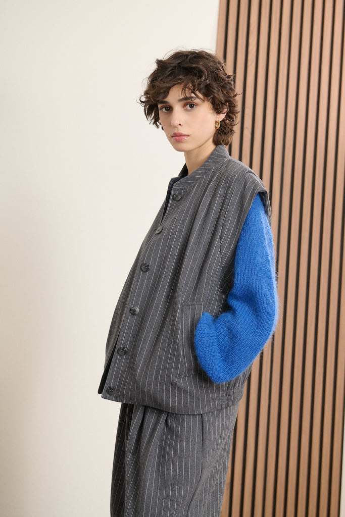 Veste courte coloris gris, sans manches, avec élastique à la taille dans le dos avec doublure et bouton effet corne.