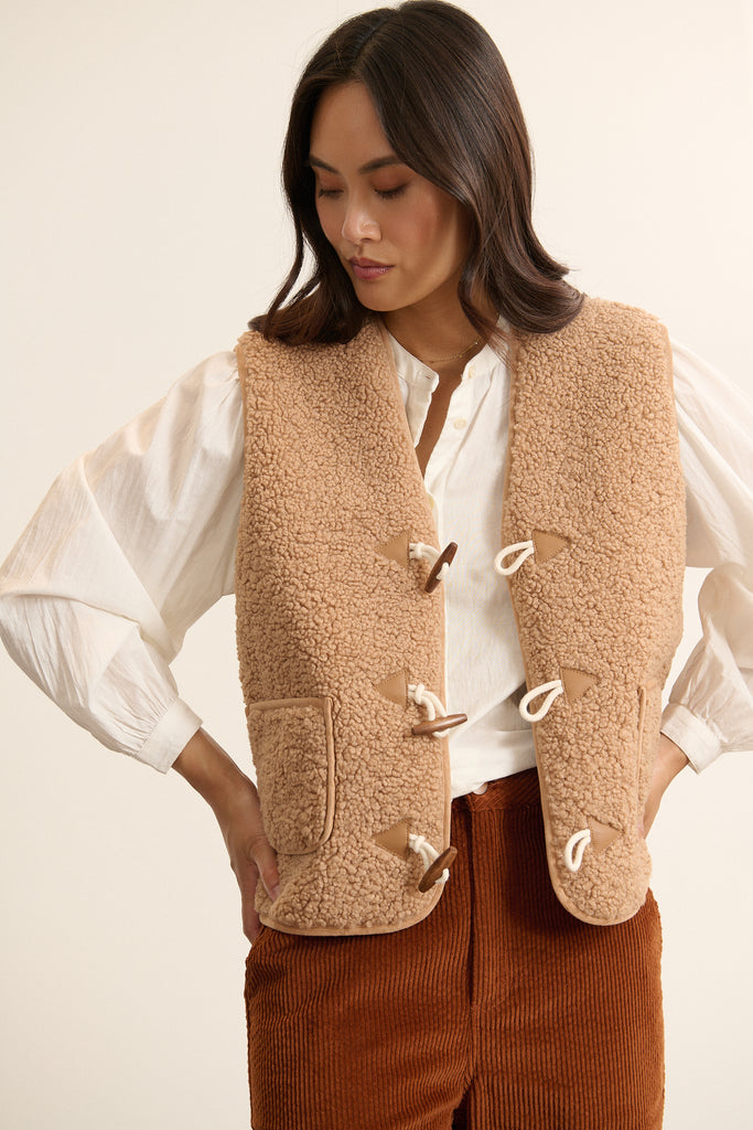 Mannequin femme de face portant une veste sans manches beige effet peau de mouton, coupe droite avec col montant.