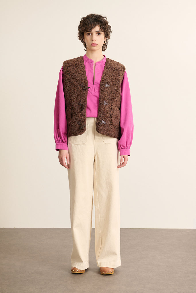 Mannequin femme de face portant une veste sans manches marron effet peau de mouton, coupe droite avec col montant.