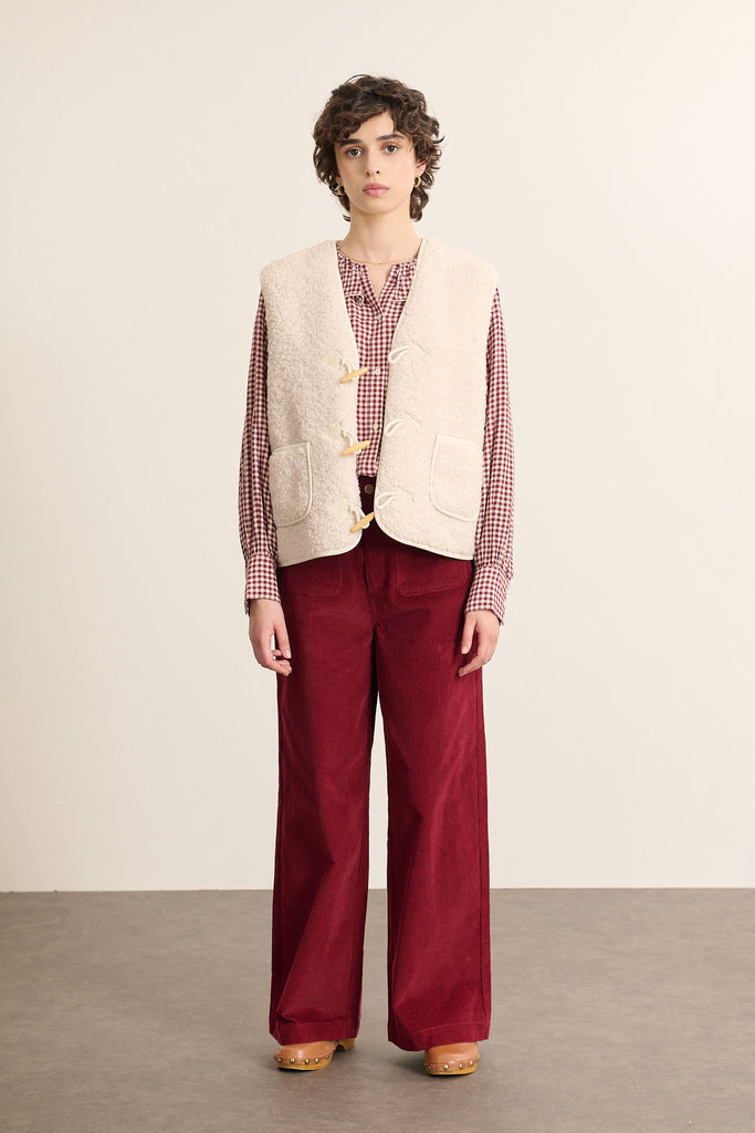 Fabriquée entièrement en polyester, veste sans manches POLETTE coloris écru avec bouton brandebourg.