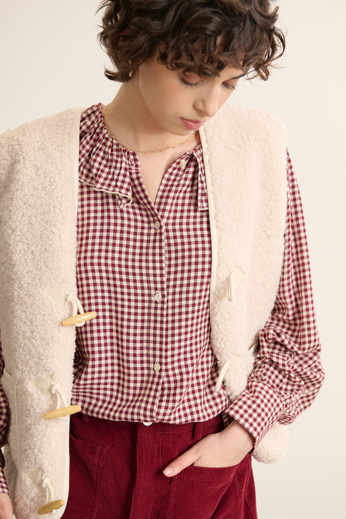 Fabriquée entièrement en polyester, veste sans manches POLETTE coloris écru avec bouton brandebourg.